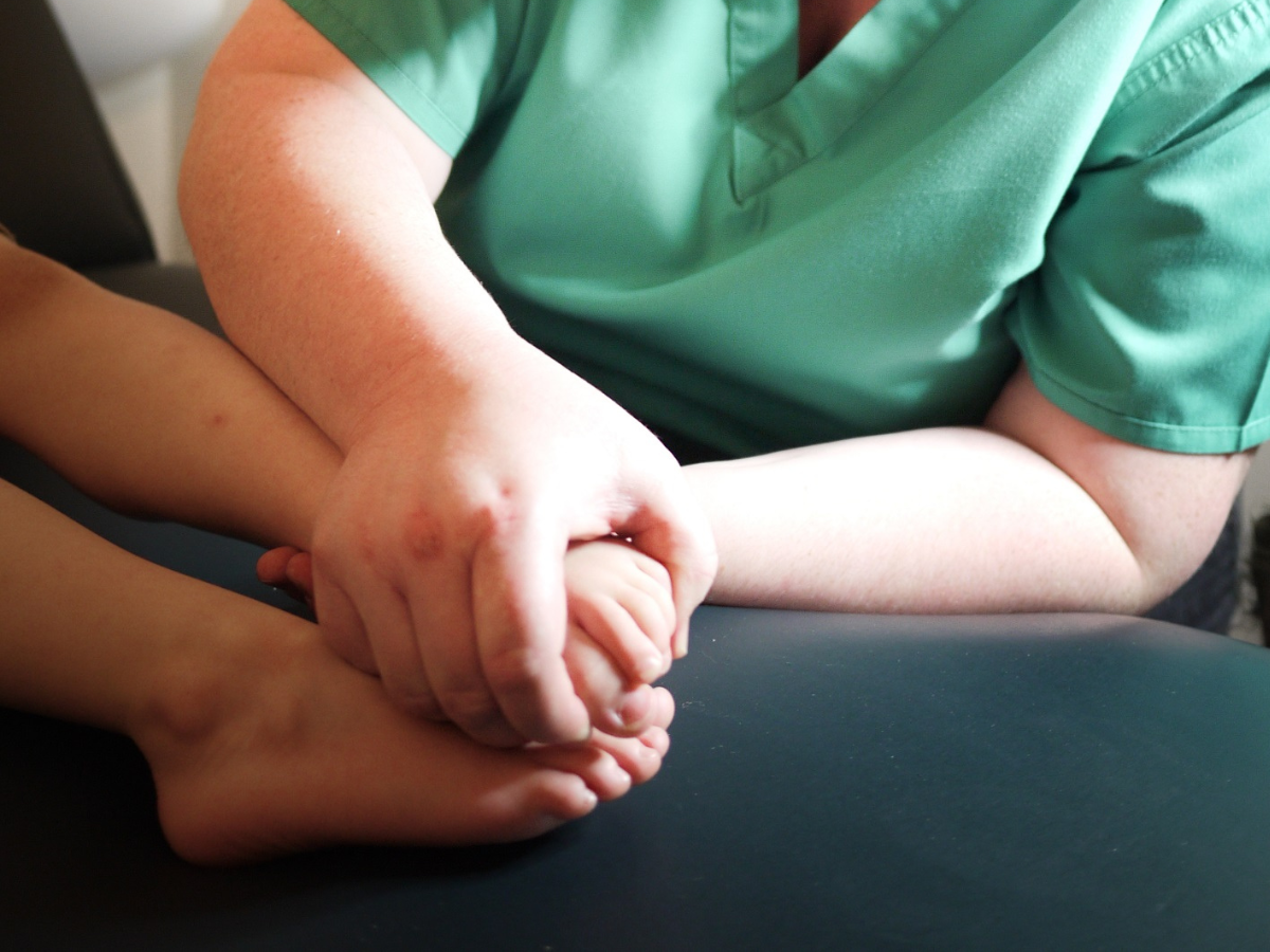Adult hands hold the digits of a child's foot. A paediatric foot examination is taking place.