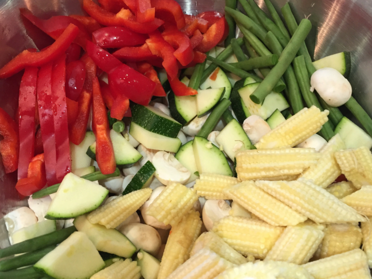 A silver container holds chopped vegetables for a stir fry: red pepper, courgettes, baby sweetcorn and mushrooms.