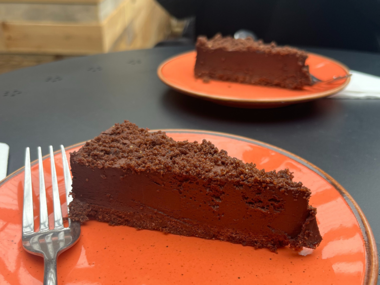 Two plates of glossy and fudgy looking chocolate cake with a crumb topping. The plates are bright orange ceramics.