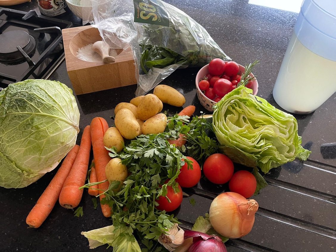 Various vegetables on a black granite kitchen counter top: carrots, baby potatoes, spinach, parsley, tomatoes, lettuce, cabbage, onions and garlic. A bowl of salt in a pestle and mortar.