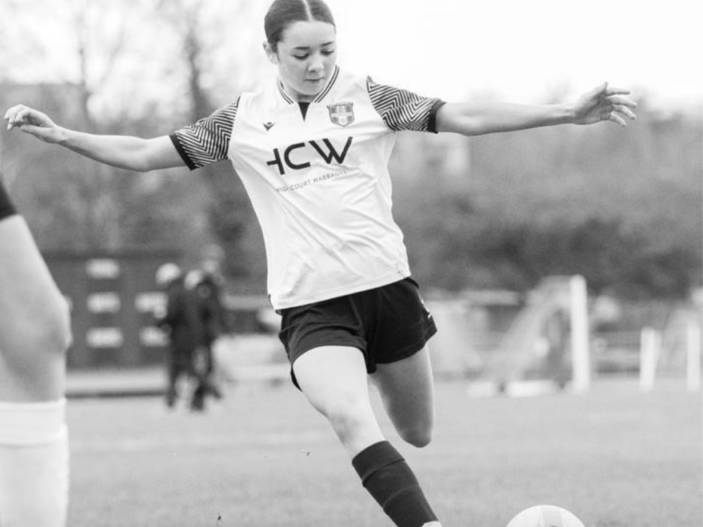 Black and white photo of a strong and confident teenage girl playing football. Her arms are in the air.