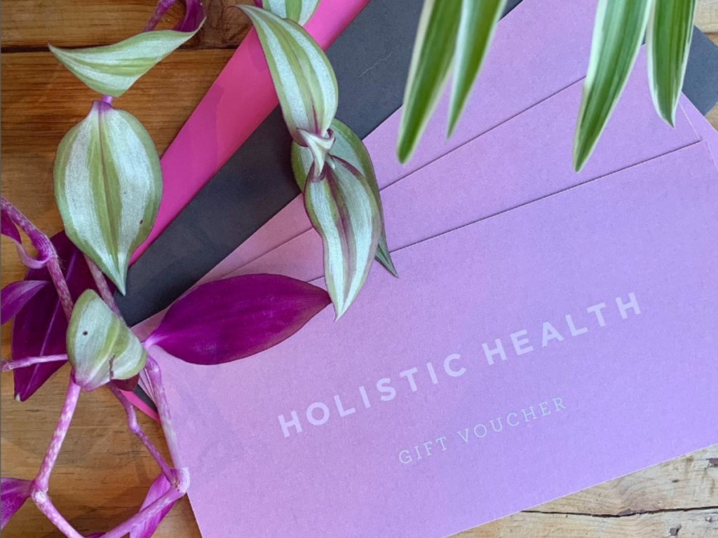 Holistic Health gift vouchers against a wooden table. There are plants overlapping the vouchers.