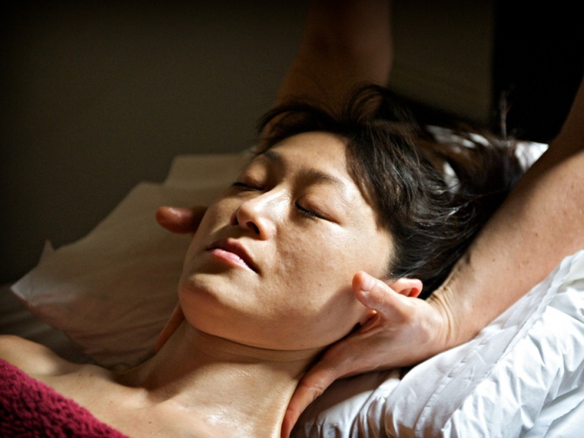 A woman's neck is being massaged. She is covered by a fluffy red towel. Her head is supported by a pillow.