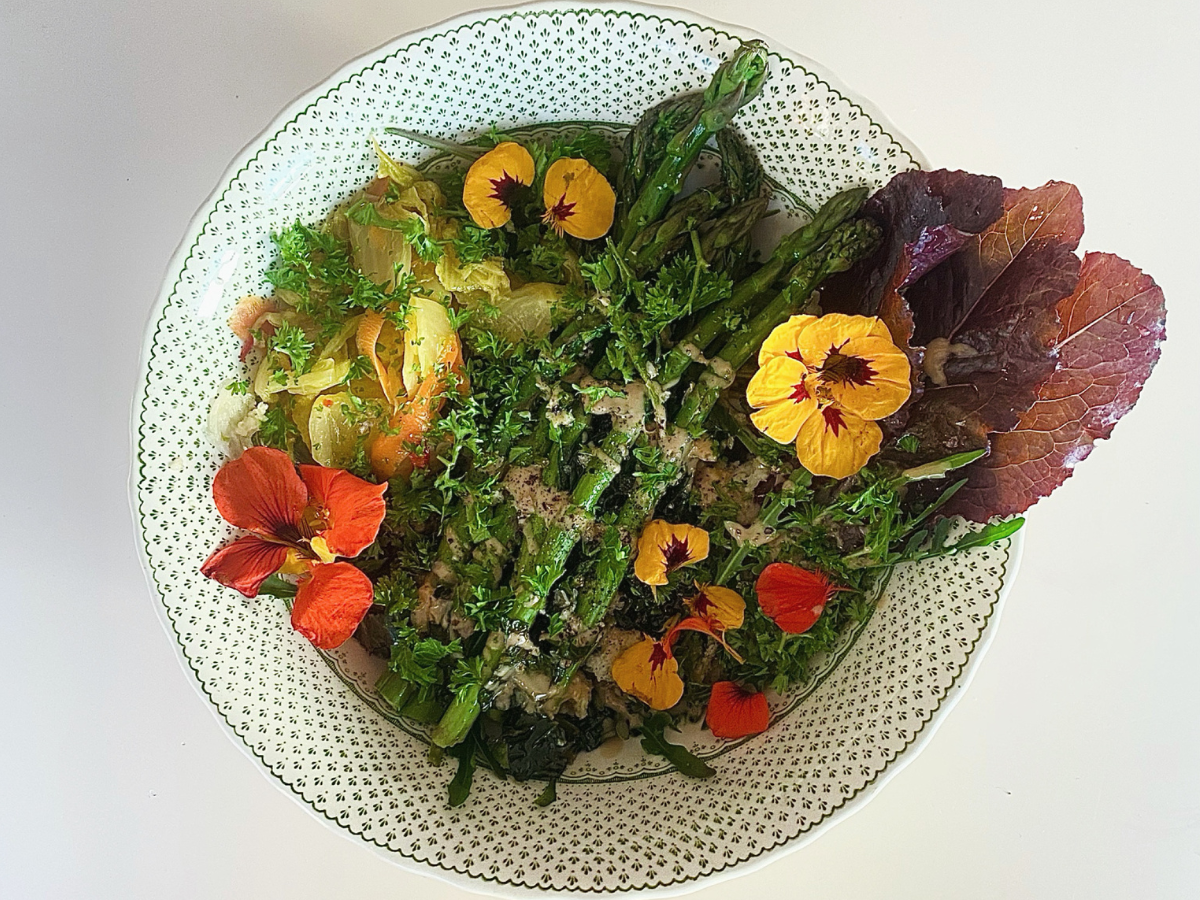 Edible flowers adorn a bowl of dressed salad. The shot is taken from above.