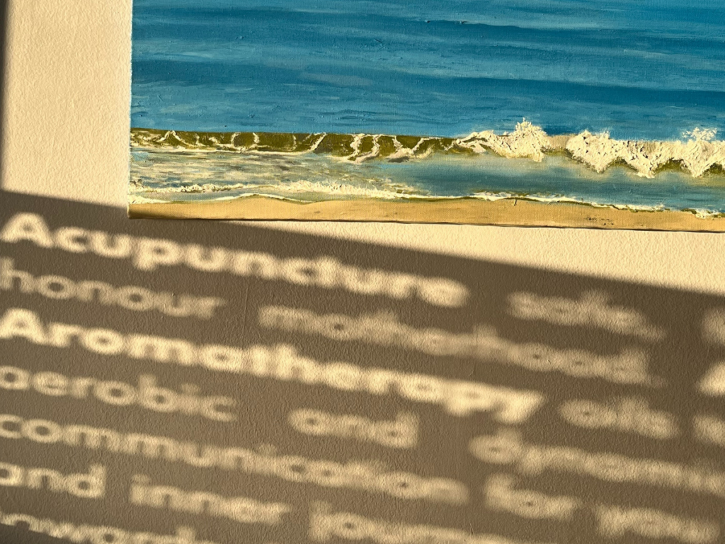 The sun shines through the window decals at Holistic Health advertising the many services of the clinic. You can read 'acupuncture' and 'aromatherapy'. A painting of waves in a blue sea hangs on the wall. summer detox
